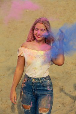 Neşeli gülümseyen sarışın kız pembe ve mavi kuru boya Holi çölde, bir bulut poz