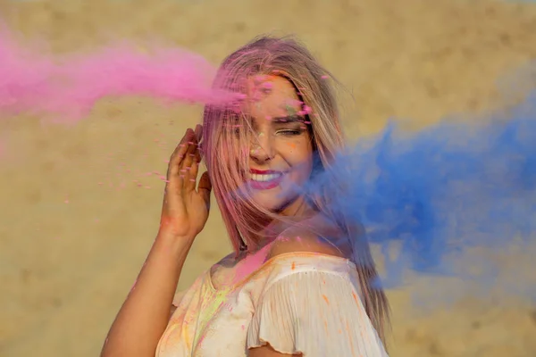 积极的金发女孩摆在粉红色和蓝色干漆的云在沙漠的节日 — 图库照片