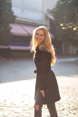 Siyah palto giyiyor ve city adlı poz uzun saçlı neşeli sarışın kadın portresi Sunny sokak