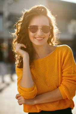 Romantik gülümseyen esmer kadın kıvırcık saçlı gözlüklü güneş ışınlarının poz