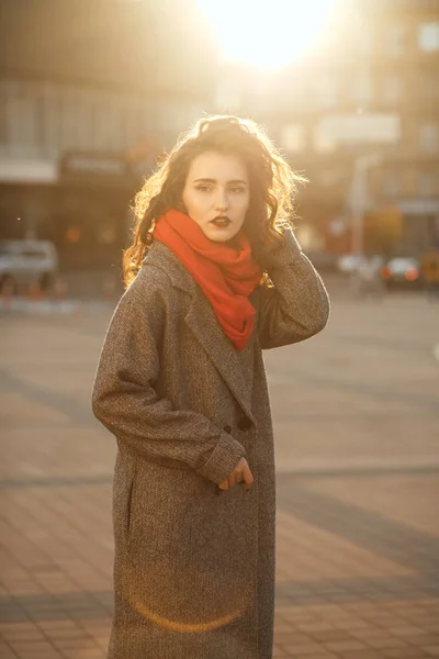 トレンディな服を着てブルネット女性波状毛のコートを着ていると太陽の光線のポーズの都市の肖像 — ストック写真