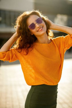 Flört genç kadın trendy kıyafeti giymiş ve güneşli Caddesi'nde yürürken güneş gözlüğü