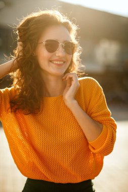 Güzel genç kadın trendy kıyafeti giymiş ve güneşli Caddesi'nde yürürken güneş gözlüğü