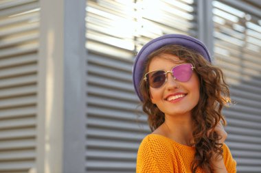 Portre portre oldukça gülümseyen esmer modeli kıvırcık saçlı mavi şapka ve gözlük takıyor. Boş alan