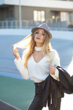 Güzel sarışın modeli şapka ve güneşli bir günde poz örme kazak giyiyor