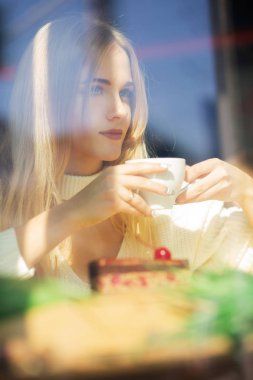 Bir fincan kahve ile restoranda vakit güzel sarışın kadın. Pencere camı delip vurdu