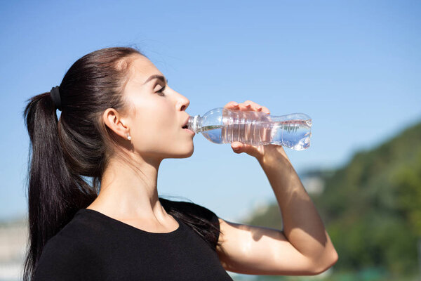 Attractive sporty woman drinking water during running at the park in sunny morning. Space for text