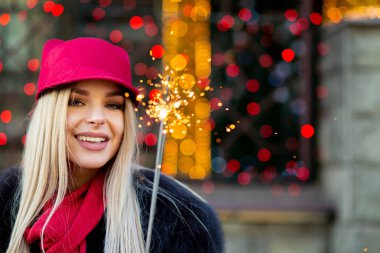 Havai fişekleri ile eğleniyor bokeh arka plan şık kış kıyafeti giymiş seksi gülümseyen sarışın kadın. Boş alan