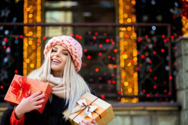Sarışın kadın çekici hediye kutuları arka plan, bokeh ışık tutarak sıcak kıyafetle giyinmiş. Boş alan