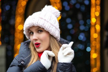 Sokağın bokeh ile bir çelenk arka plan üzerinde poz örme şapkası kırmızı ruj ile neşeli sarışın kadın