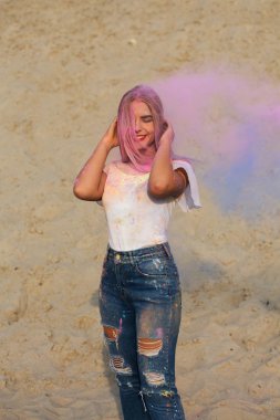 Neşeli sarışın kadın giyiyor beyaz t gömlek ve kot pantolon, pembe ile oynarken Holi boya çöl, Kuru