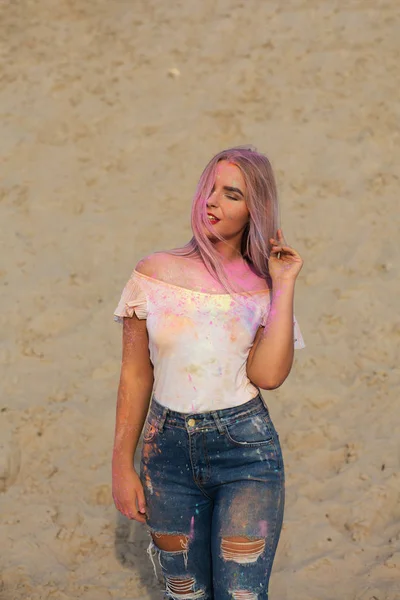 Muhteşem sarışın kadın giyiyor beyaz t gömlek ve kot pantolon, pembe ile oynarken Holi boya çöl, Kuru