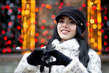 Güzel romantik kız bir kalp yapma hareketi ile parmaklarını garland arka plan üzerinde