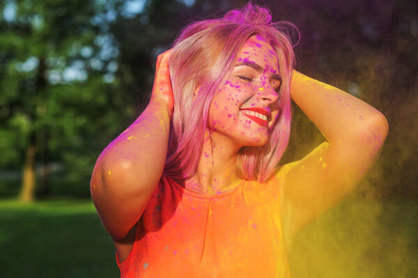 Веселая блондинка развлекается с красочной сухой краской в парке. Концепция фестиваля Холи
