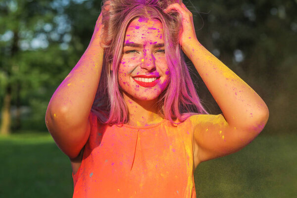 Радостная блондинка развлекается с красочной сухой краской в парке. Концепция фестиваля Холи
