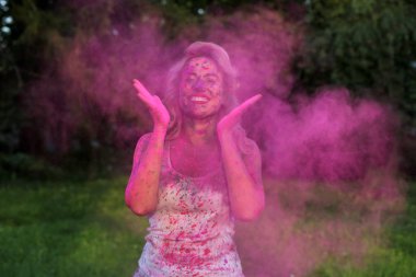 Parkta bir bulut pembe kuru Holi boya ile eğleniyor olumlu genç kadın portresi