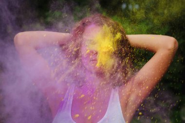 Onun yanında patlayan mor ve sarı kuru Holi boya ile oynayan beyaz t gömlek giyen genç redhaired kadın