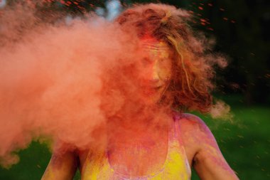 Etrafındaki turuncu kuru Holi boya ile oynayan beyaz t gömlek giymiş neşeli redhaired kız
