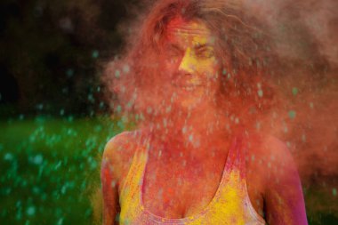 Etrafındaki turuncu kuru Holi boya ile oynayan beyaz t gömlek giyen serin redhaired kadın