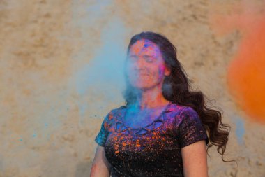 Uzun kıvırcık saçlı turuncu ve mavi kuru Holi toz patlayan ile oynarken mutlu esmer kadın 