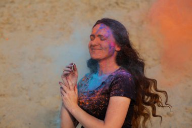 Turuncu ve mavi kuru Holi toz patlayan ile oynarken uzun kıvırcık saçlı esmer kadın memnun 