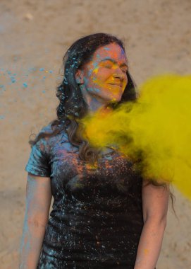 Uzun kıvırcık saçlı sarı kuru Holi toz patlayan ile oynayan neşeli esmer kadın 