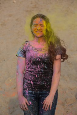 Happy brunette woman enjoying Holi festival at the desert. Woman posing with exploding yellow paint