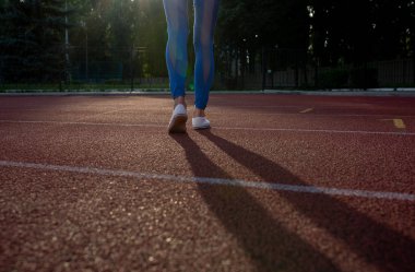 Mavi tozluk güneşli gece boyunca stadyum üzerinde çalışan kadın bacaklarını açıp closeup çekim izlemek. Metin için yer