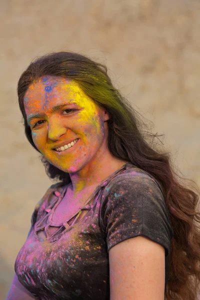Attractive brunette woman with long wavy hair wearing black t shirt covered with colorful dry powder Holi at the desert