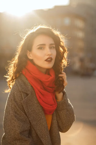 Stylish brunette woman with lush hair posing in soft evening backlight at the avenue