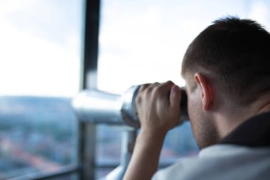 Young man looking through binoculars to the landmark panorama from the observatory. Copy space