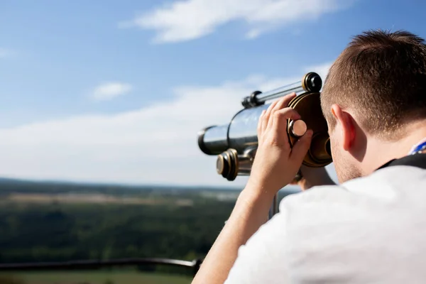 Young man looking through binoculars to the landscape panorama. Space for text