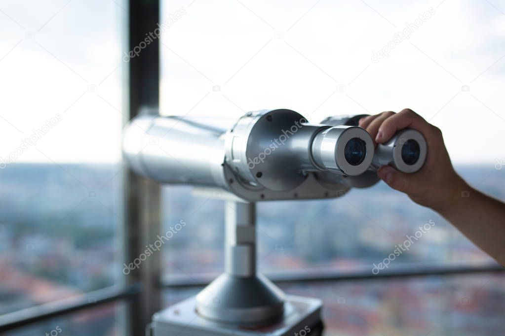 Male hand holding binoculars against the landmark panorama from the observatory. Closeup shot