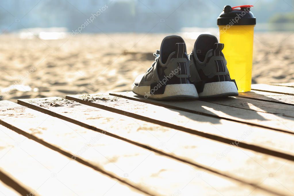 Closeup shot of woman's sneakers and water bottle standing on the beach. Copy space