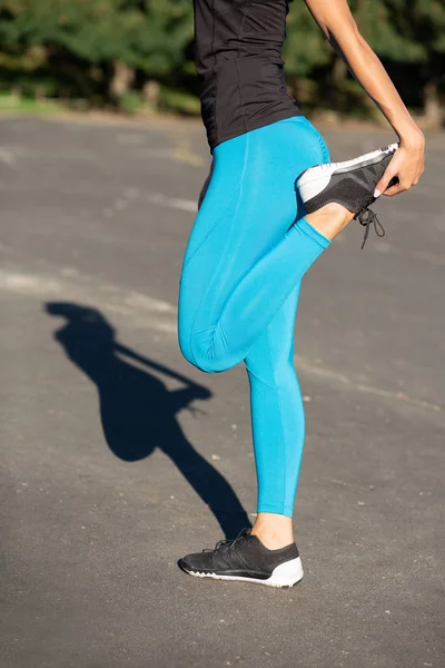 Fit young woman wearing sport apparel, stretching before training at the stadium