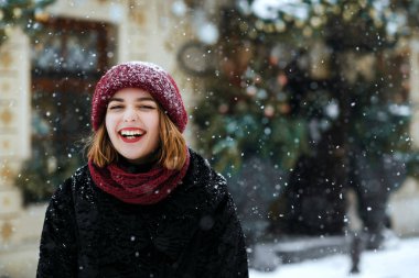 Kırmızı bere sokağın kar yağışı sırasında poz giyen neşeli esmer kadın. Boş alan
