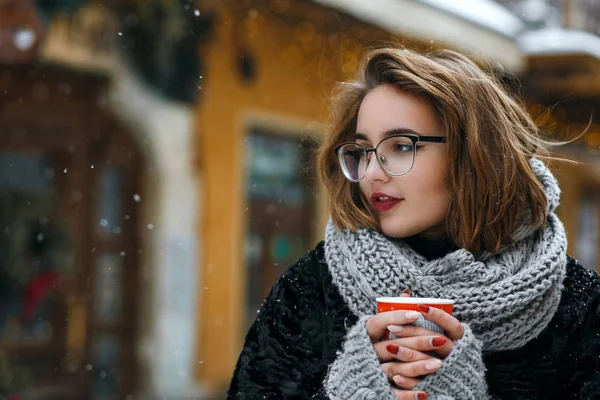 Winter outdoor portrait of romantic brunette woman wearing glasses drinking coffee at the street. Space for text