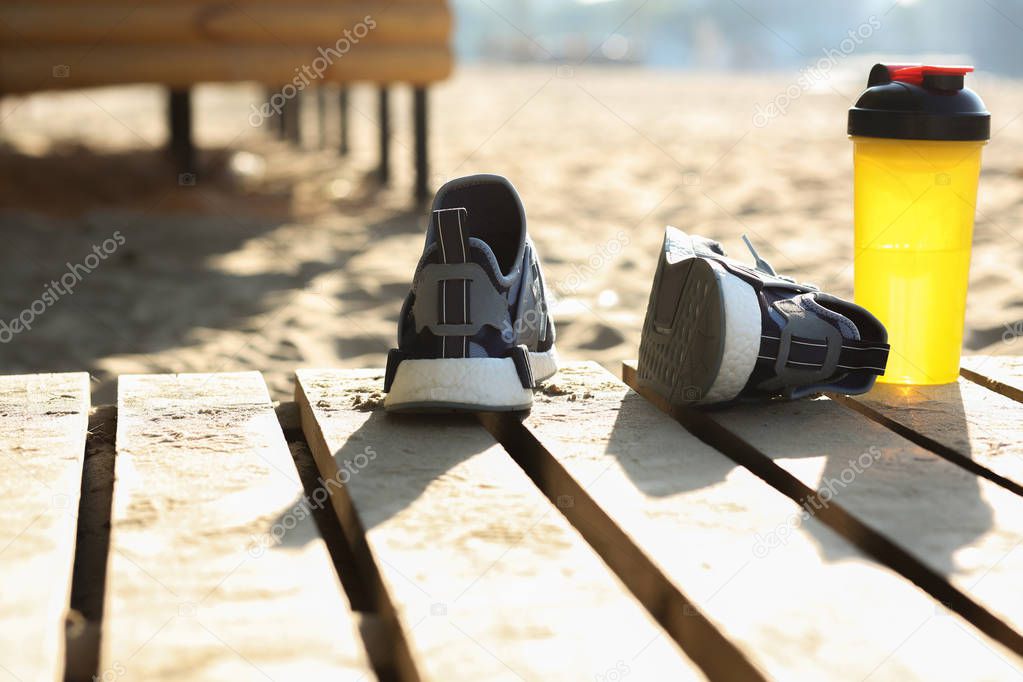 Closeup shot of female sport shoes and water bottle standing on the beach. Space for text
