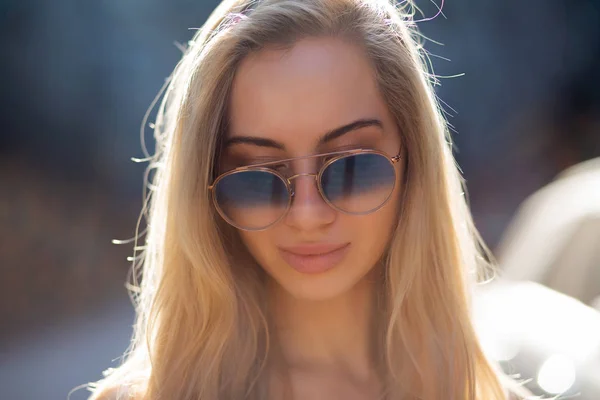 Pretty young woman with long hair wearing glasses, posing at the street in sunny day