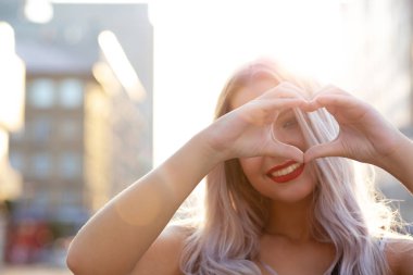 Kırmızı dudaklar sokağın parmakları ile kalp şekil verme ile neşeli sarışın kadın. Metin için yer