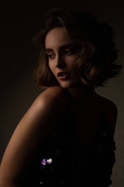 Şanlı esmer kadın kıvırcık saçlı kontrast stüdyoda ışık ile poz parlak elbise giyer