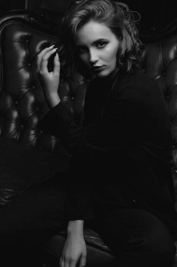 Güzel genç kadın uzun saçlı vintage kanepede poz ceket giyiyor. Siyah ve beyaz tonlama