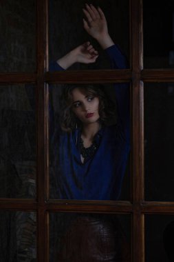 Bluz ve cam kapının arkasında poz kolye giyen kıvırcık saçlı güzel esmer modeli