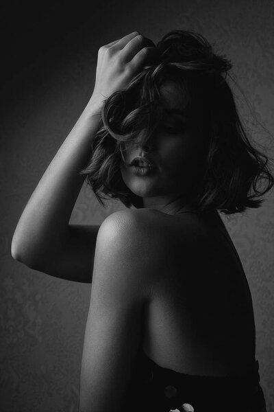 Black and white portrait of seductive brunette woman with naked shoulders posing with dramatic light