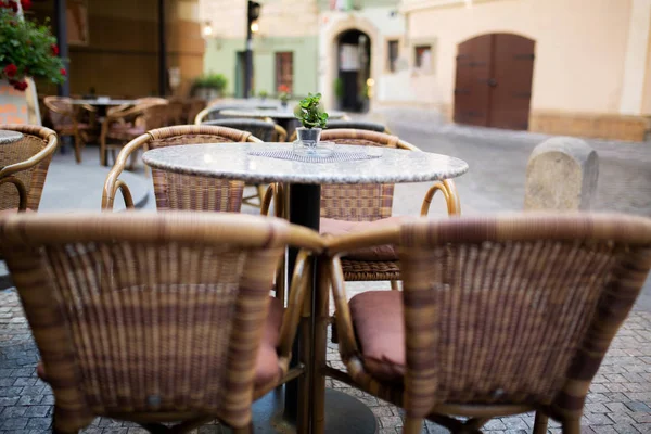 Empty rattan chairs and tables outside a street restaurant in Prague