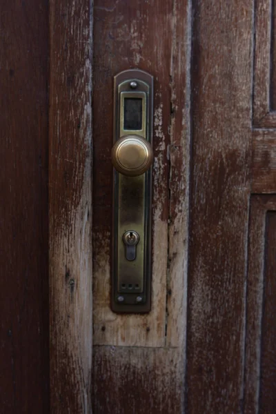 Bronze iron door handle of a brown scratched door. Closeup photo