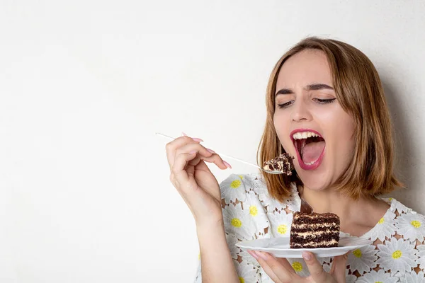 Bastante joven comiendo sabroso pastel de chocolate sobre fondo blanco —  Fotos de Stock