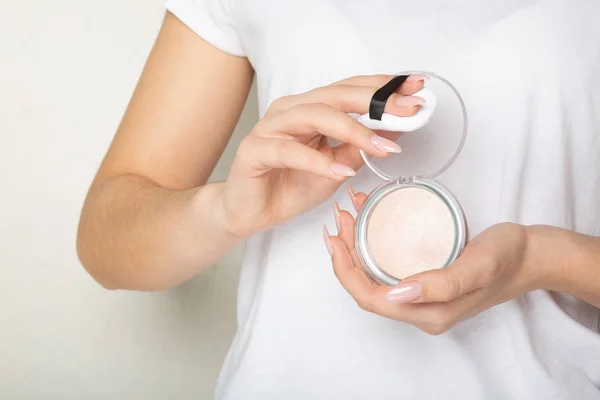 Female hands holding highlighting powder with a puff over a whit