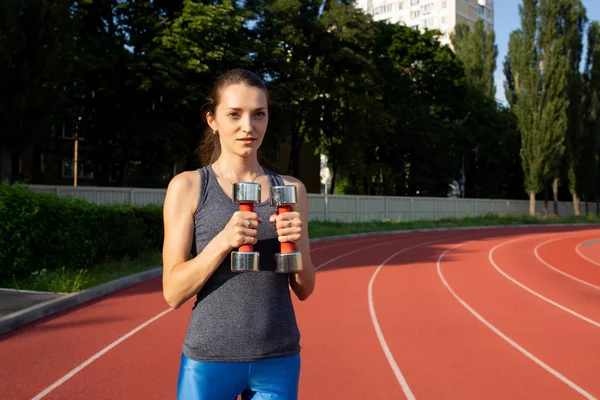 Mujer bastante en forma haciendo ejercicios con pesas en el estadio — Foto de Stock