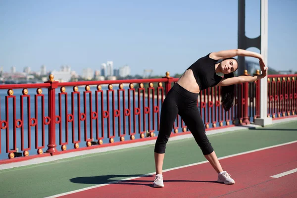 Lovely fitness woman stretching at the pedestrian bridge before